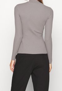 Figurbetontes, langärmeliges Oberteil aus grauem Rippstoff mit hohem Kragen. Glatte Textur und ein elegantes Design. Kombiniert mit schwarzen Hosen.