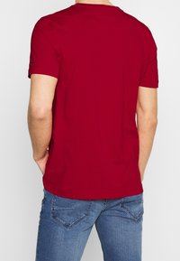 Červené bavlněné tričko s krátkým rukávem, kulatým výstřihem a rovný střih. Zadní pohled ukazuje hladkou texturu a žádné viditelné vzory.