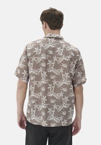 Camisa de manga corta, color marrón claro, con un estampado de hojas de palma en color blanco roto. Fabricada con una tela texturizada, tiene un corte relajado y un cuello.