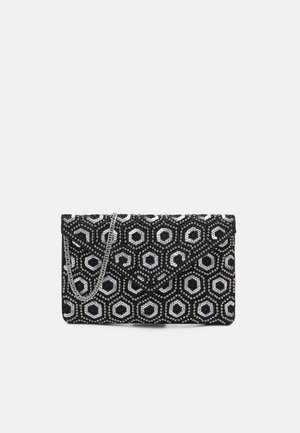 Schwarze Clutch mit silbernem sechseckigem Perlenmuster und dünnem silbernen Kettenriemen auf einfarbigem Hintergrund.