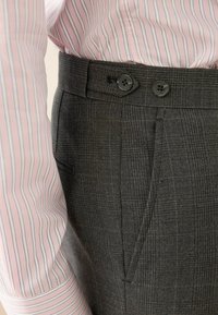 Pantalon gris à motifs avec une finition texturée, doté de deux boutons à la taille, de poches latérales, et d'une manche de chemise rayée rose et blanche.