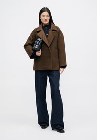 Καφέ παλτό σε ψαροκόκαλο με μεγάλα πέτα, συνδυασμένο με σκούρο πλεκτό τοπ, μπλε φαρδιές παντελόνα και μικρή μαύρη τσάντα.