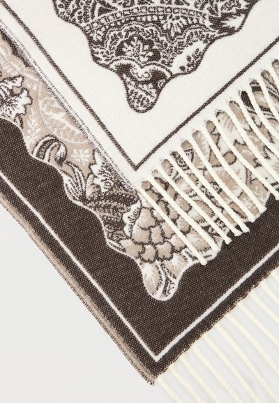 Gros plan sur un tissu tissé beige et brun à motifs superposés avec des motifs floraux complexes et des bords à franges torsadées.