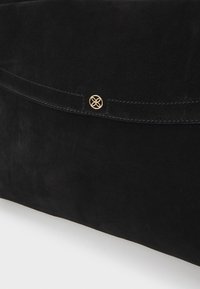 Svart semsket clutch-veske med en glatt overflate, klaffelukking og en gullfarget knapp med intrikat design.