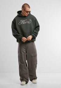 Dark green hooded sweatshirt with a large graphic print, paired with loose, gray cargo pants featuring multiple pockets and a relaxed fit.