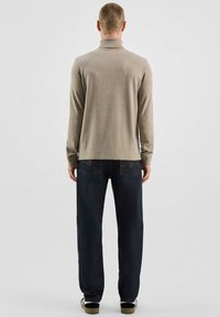 Beżowy sweter z golfem wykonany z miękkiego materiału, w połączeniu z ciemnoniebieskimi, luźnymi dżinsami. Prosty design z minimalnym zdobieniem.