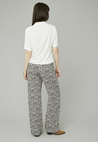 Haut blanc à manches courtes associé à un pantalon large noir et blanc à motifs. Le pantalon présente un motif léopard.