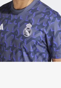 Tmavě fialový a černý vzorovaný fotbalový dres Real Madrid s logem Adidas na hrudi, nošený osobou, ustřižený na krku a rukávech.