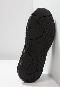 Black athletic shoe sole with textured patterns, grip elements, and a smooth area; features a logo near the heel.
