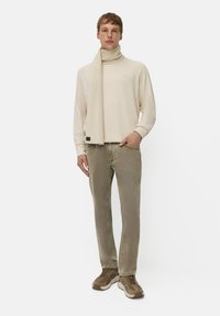 Beige langærmet top med ribbet tørklæde, oliven grøn jeans med afslappet pasform og brune sneakers med strukturerede detaljer.