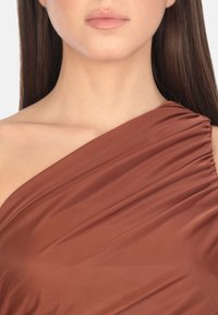 Vestito marrone a spalla unica realizzato in tessuto liscio, con dettagli drappeggiati e accenti arricciati lungo la spalla.