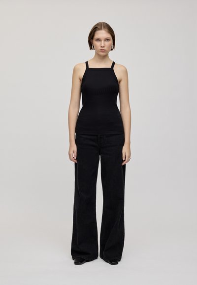 Zwarte mouwloze top met een vierkante halslijn, gecombineerd met hoge zwarte wijde jeans met een subtiele textuur en een gladde afwerking.