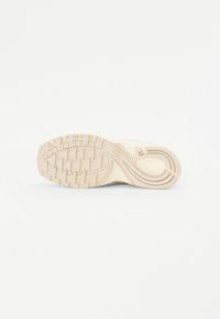 Semelle de chaussure de sport en beige clair avec un design texturé comportant des motifs en zigzag, des rainures et des accents de rembourrage ronds.