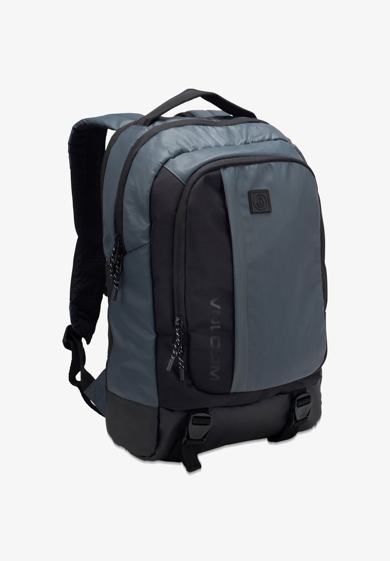 Backpack in blue-grey and black, featuring padded straps, textured fabric, multiple zip pockets, and a logo accent on the front.