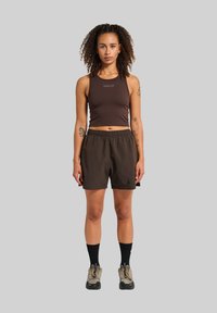 Hnedý crop tank top s logom "HALO", spárovaný s hnedými šortkami, čiernymi členkovými ponožkami a béžovými teniskami s čiernymi podrážkami.