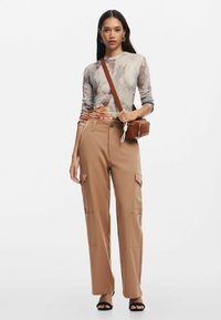 Maglia a maniche lunghe multicolore con motivo floreale; pantaloni cargo beige con tasche laterali; borsa a tracolla marrone; tacchi aperti neri.