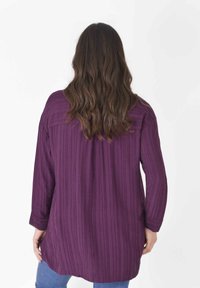 Blusa viola a maniche lunghe, morbida e con vestibilità ampia, caratterizzata da righe verticali, orlo arrotondato e texture morbida. La vista posteriore mostra una silhouette rilassata e la cucitura della spalla.