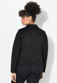 Black faux suede jacket with a classic collar, epaulets, and zippered cuffs. Features a belted waist and smooth texture for comfort.