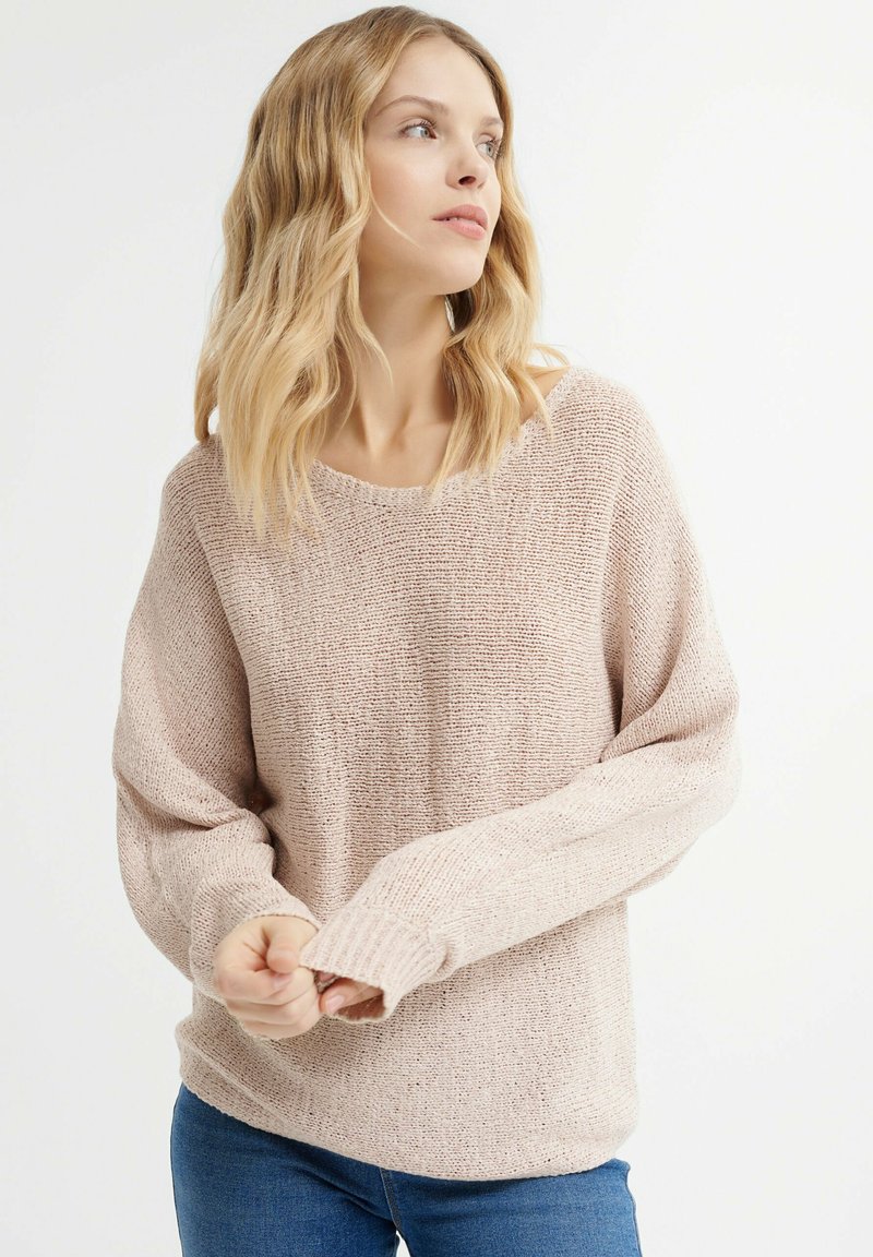 Light pink knit sweater with a loose fit, wide round neckline, and ribbed cuffs. Its texture features a subtle open weave pattern.