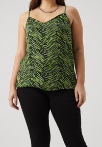 Vihreä ja mustapilkullinen camisole ohuilla hihnoilla ja v-pääntiellä, yhdistetty mustiin istuviin housuihin. Ketjukaulaketju yksityiskohtana.