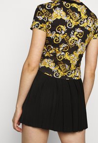 Czarna spódnica plisowana zestawiona z bluzką z krótkim rękawem, zdobioną złotym i białym wzorem na czarnym tle.