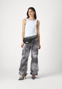 Hvit uten ermer topp med nagledetaljer, kombinert med løse grå tie-dye bukser og en svart midjeveske. Svarte pumps fullfører antrekket.