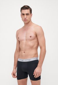 Black boxer briefs with a grey elastic waistband featuring the brand name "ellesse" printed on it. Smooth, stretchy fabric, fitted design.