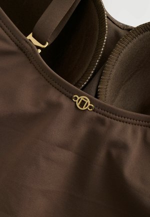 Bra in Braun mit glatter Oberfläche, vorgeformten Cups, verstellbaren Trägern und einem goldfarbenen Logo-Detail nahe dem Ausschnitt.
