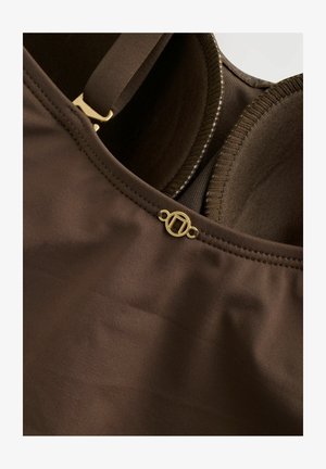 Sostenedor marrón con tejido suave, copas moldeadas, tirantes ajustables y un detalle de logo en tono dorado cerca del escote.