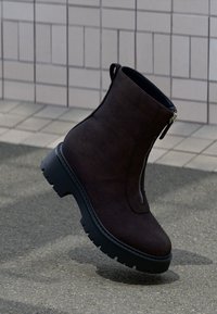 Dark brown suede ankle boot with a side zipper, chunky black sole, and minimalistic design. Soft texture with a clean silhouette.