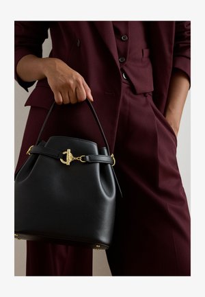 Bordó öltönyt viselő személy fekete bőr kézitáskát tart arany színű kapoccsal és felső fogantyúval az oldalán.