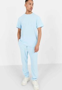 Hele sinine ribatud t-särk ja sobivad dressipüksid elastsete varrukatega, koos valgete tossudega. Kangas on pehme ja siledapindne.