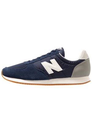 Navy blue and gray athletic sneaker with white "N" logo, lace-up closure, and gum rubber sole, side view on white background.