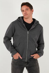 Grå zip-up hoodie med dragsko på huvan, kängurufickor och ribbade muddar. Bärs över en svart skjorta och matchas med mörka jeans.