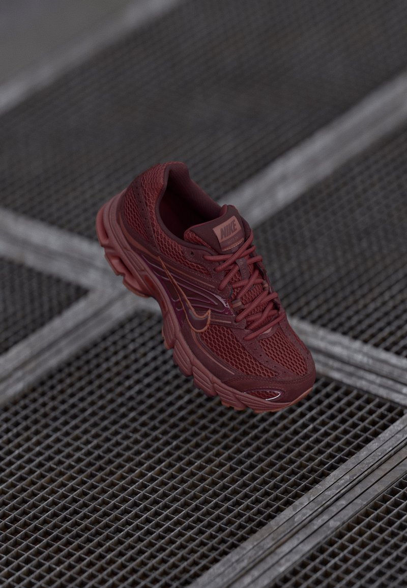 Červená bežecká obuv Nike s sieťovaným zvrškom, textúrovanými detailmi, polstrovaným golierom a hrubou podrážkou, umiestnená nad mriežkovaným povrchom.