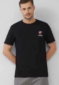 Czarna bawełniana koszulka z krótkim rękawem, okrągłym dekoltem, z grafiką czerwonego mięsa i napisem "SPOTKAJMY SIĘ NA GRILLU!" na piersi.