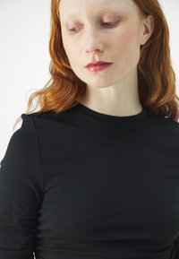 Czarny dopasowany top z okrągłym dekoltem, długimi rękawami i subtelnymi detalami na ramionach. Gładka faktura, dopasowany krój i minimalistyczny styl.