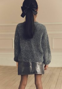 Szary, puszysty sweter z okrągłym dołem, w zestawieniu z błyszcząca, czarną spódnicą dżinsową z dwoma tylnymi kieszeniami i lekko rozszerzanym krojem.