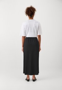 Vit bomullströja med en avslappnad passform, kombinerad med en lång svart jerseykjol. Kjolen har resårmidja och en mjuk textur.