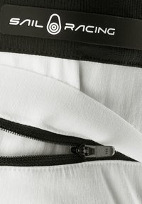Sail Racing valkoinen ja musta vetoketjullinen vaate tekstuuripinnalla, jossa on huomattava logoetiketti ja musta vetoketju.