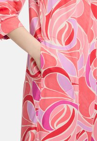 Blumenmuster-Kleid mit großen rosa und roten Wirbeln, aus glattem Stoff gefertigt und mit seitlichen Taschen ausgestattet. Elegantes Design mit umgeschlagenen Ärmeln.