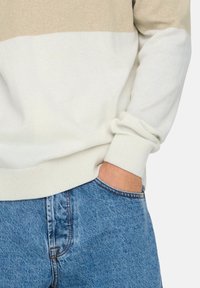 Pull en maille à rayures beiges et blanches, avec poignets et ourlet côtelés. Associé à un jean en denim bleu clair.