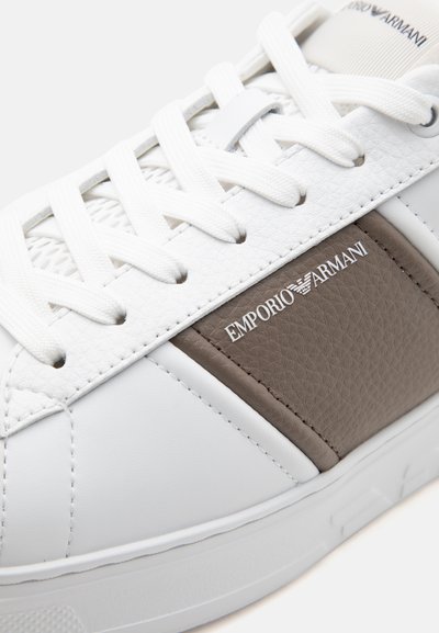 Baskets blanches avec un panneau beige texturé et le logo Emporio Armani, avec des lacets blancs et des détails en cuir cousus.
