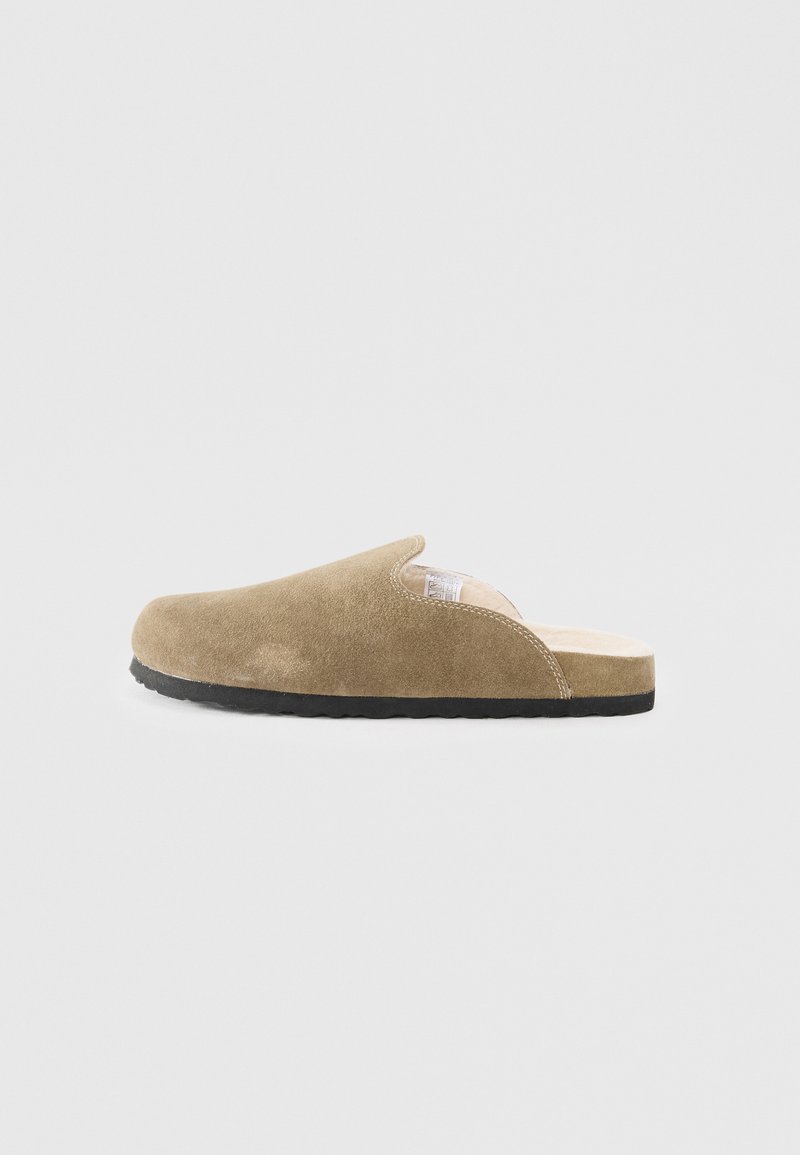 Suede slip-on slipper in beige, featuring a rounded toe, soft texture, and a rubber sole with a subtle tread pattern.