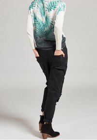 Camicia a maniche lunghe con stampa di foglie di palma verde su uno sfondo sfumato, abbinata a pantaloni tapered neri e logori e stivaletti.
