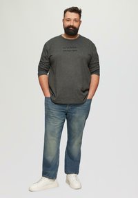 Lichtgrijze sweatshirt met lange mouwen en een gespikkeld patroon, zwarte tekst, gecombineerd met vervaagde blauwe recht-toe-rechtdoor jeans en witte sneakers.