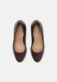 Bailarinas de piel burdeos con una textura suave, puntera redondeada, plantilla acolchada con perforaciones y letras doradas de la marca visibles.