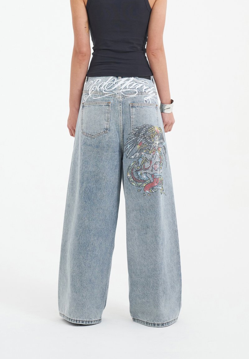 Jasnoniebieskie dżinsy o szerokich nogawkach mają haftowany wzór smoka w żywych kolorach na tylnej kieszeni. Wysoki stan z graficznym pasem.