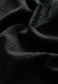 Tissu noir avec des plis doux et une texture subtile sous un éclairage diffus, mettant en valeur la surface lisse et légèrement côtelée du matériau.