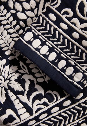 Marine stof met ingewikkelde witte borduursels met bloem- en geometrische patronen, die textuursteken en gelaagde ontwerpelementen tonen.